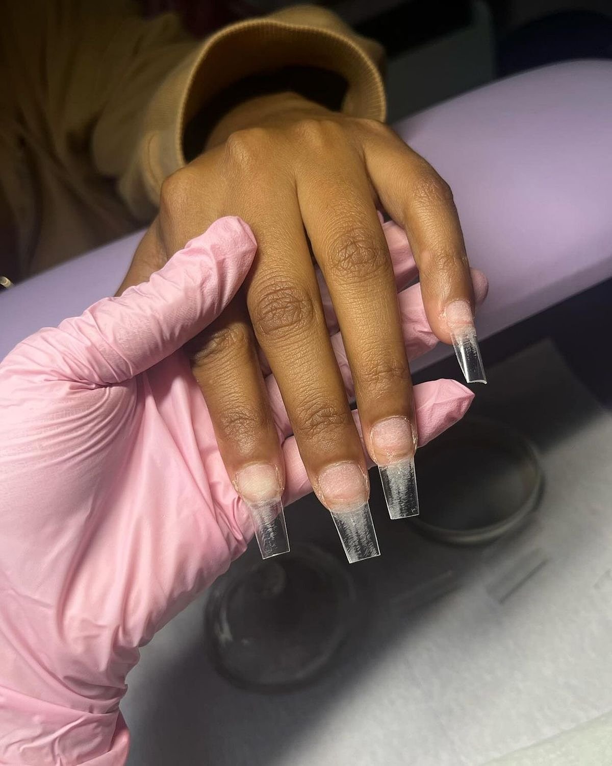 Close-up view of beautiful long clear acrylic nails displayed against a soft background.