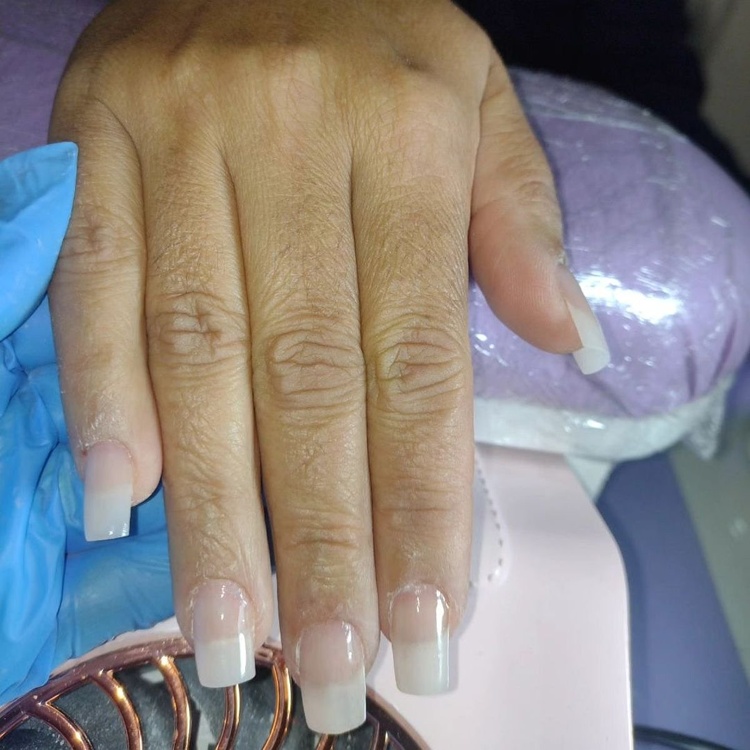 Close-up of elegant light pink and white acrylic nails on a hand against a soft background.