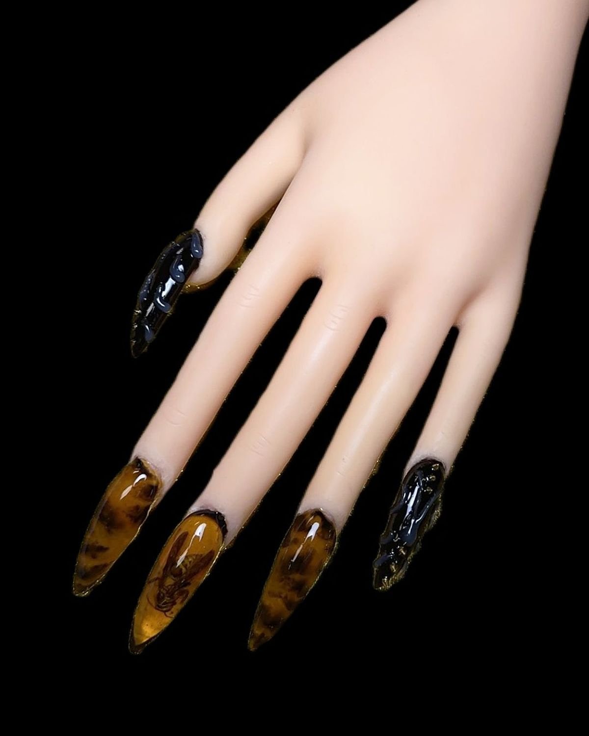 This image features a long, elegant hand with black and amber nails showcasing unique glossy finishes.