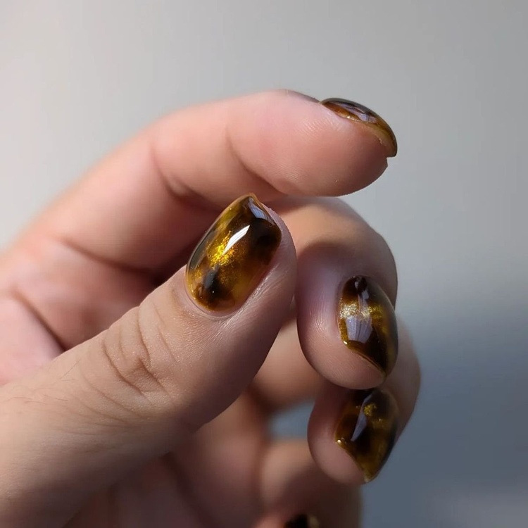 A close-up of amber gold nails with a shiny finish, showcasing a unique design.