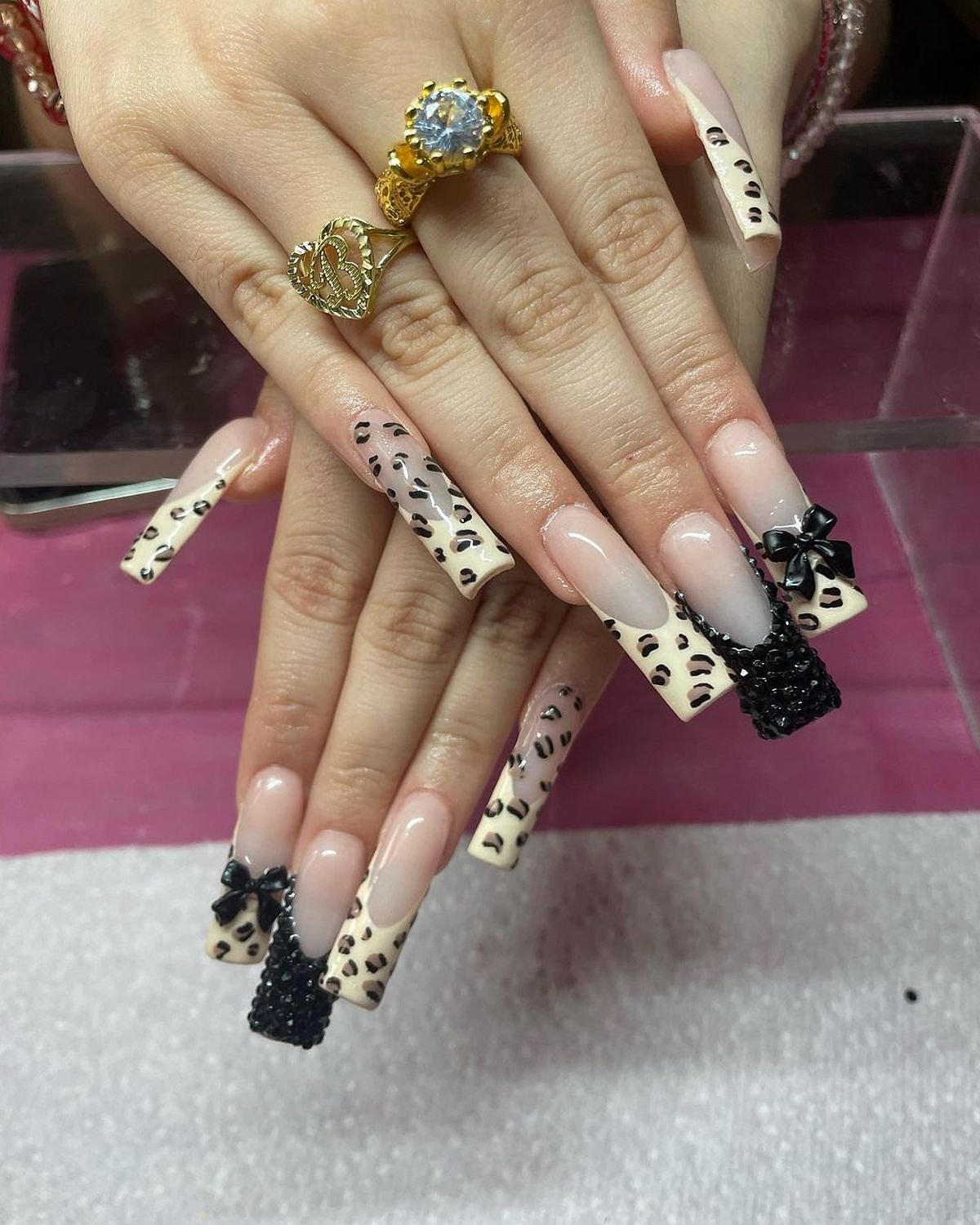 Elegant long nails with pink and black animal print design, featuring intricate detailing and embellishments.