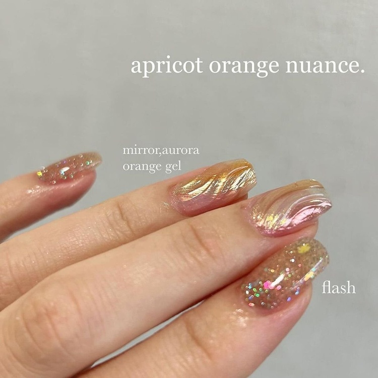 A close-up view of beautiful apricot orange nails adorned with glitter and a mirror finish, showcasing intricate designs and a luxurious look.