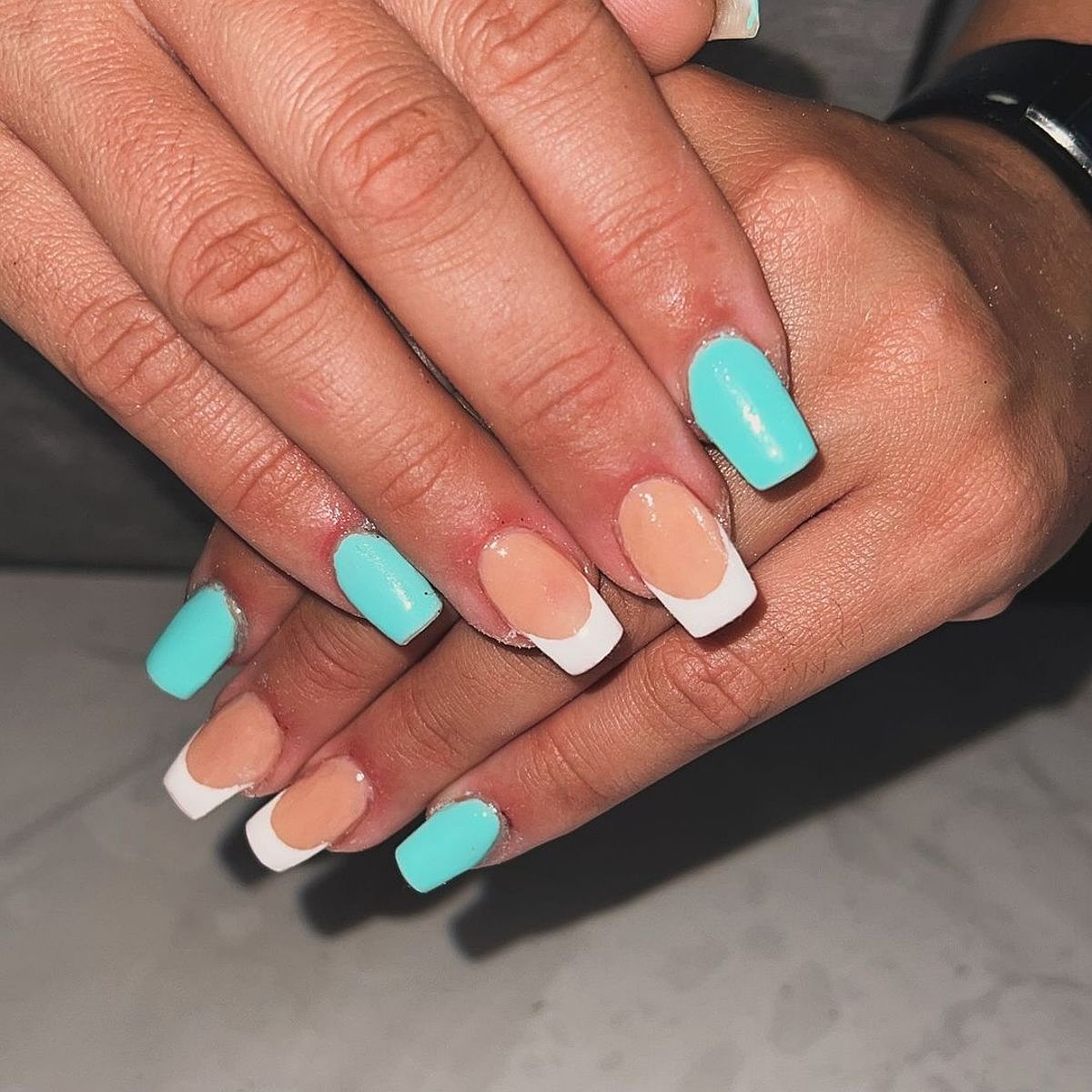 Two hands with aqua and peach nails featuring stylish white tips on a neutral surface.