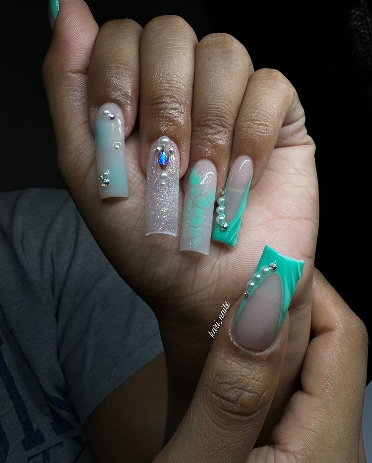 A pair of hands showing beautifully designed aqua and glitter nails, featuring decorative accents.