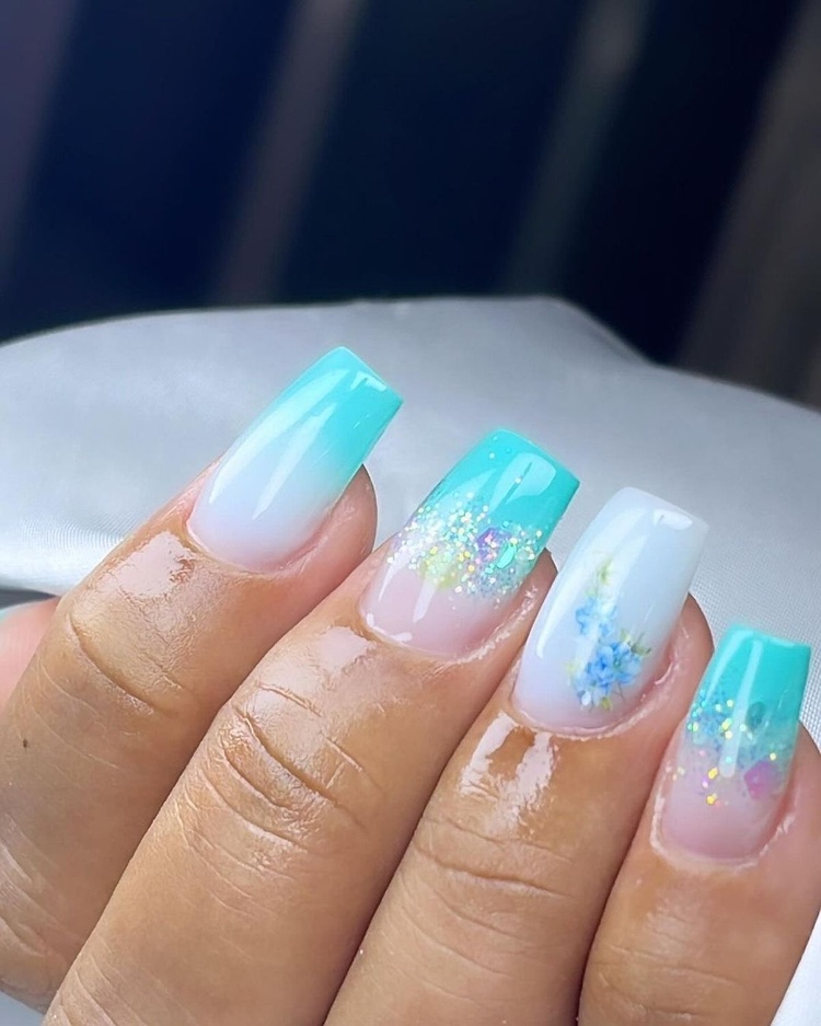 Close-up of elegant aqua and white French tip nails with glitter accents, showcasing a floral design.