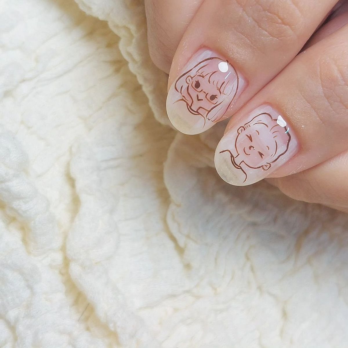 Close-up of delicate pink nails featuring adorable baby face designs, showcasing a creative nail art approach.