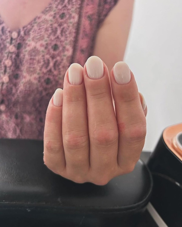 A hand with light pink nails, displaying a neat manicure against a soft background.