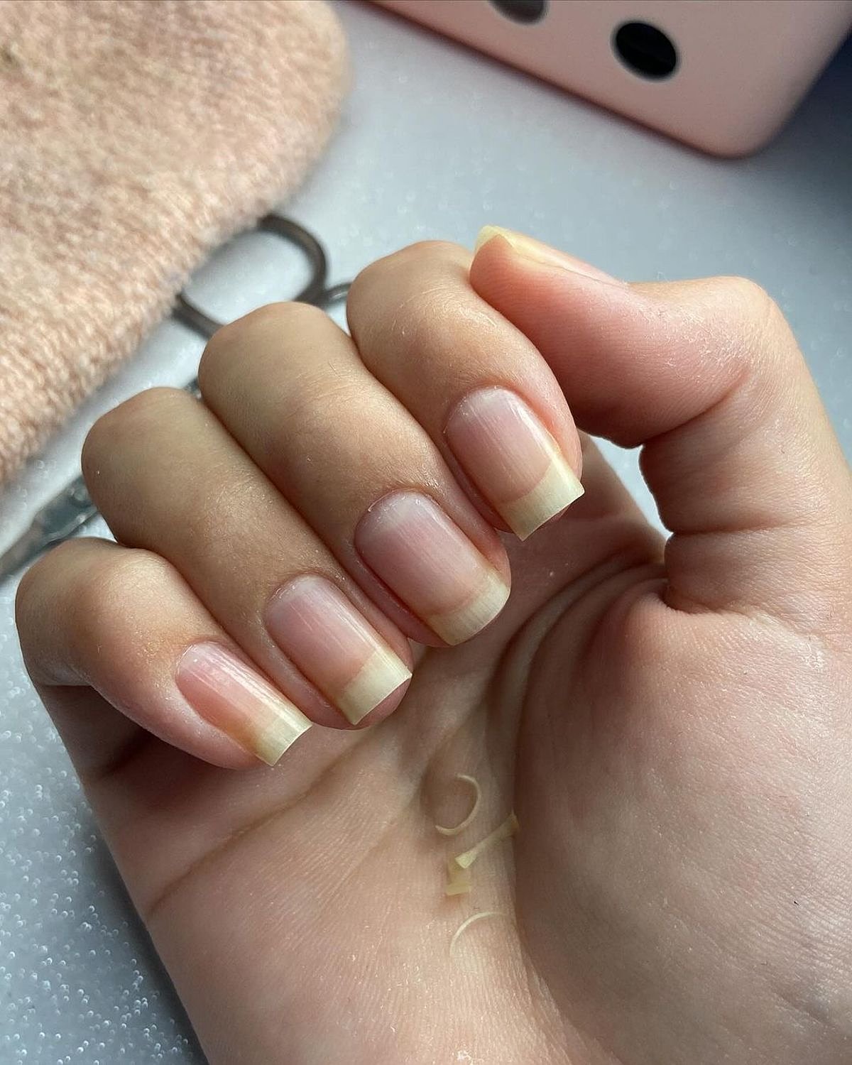 Close-up of a hand displaying nude nails with elegant white tips, set against a soft background.