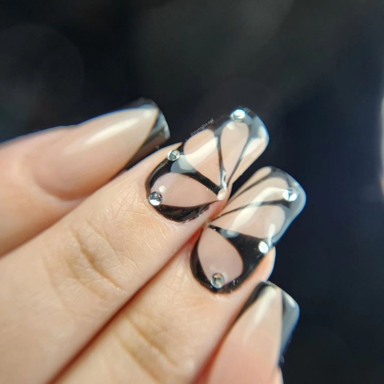 A close-up of stylish beige and black nails featuring elegant accents and details.