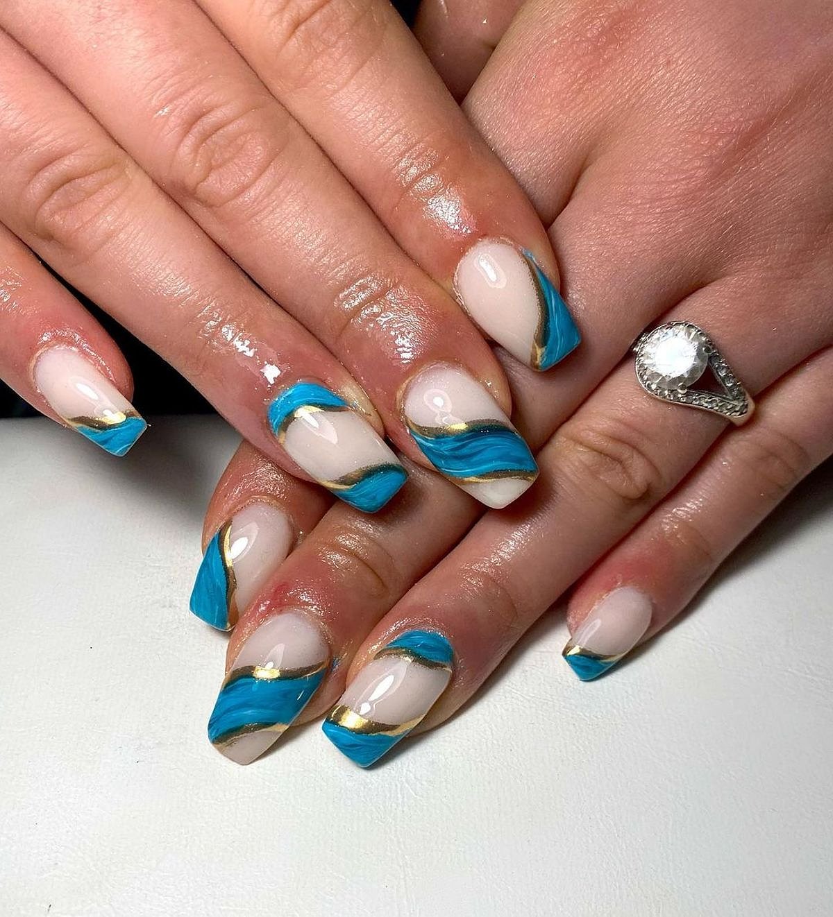 A beautiful nail design featuring beige, blue, and gold colors, showcasing intricate nail art with a glossy finish.