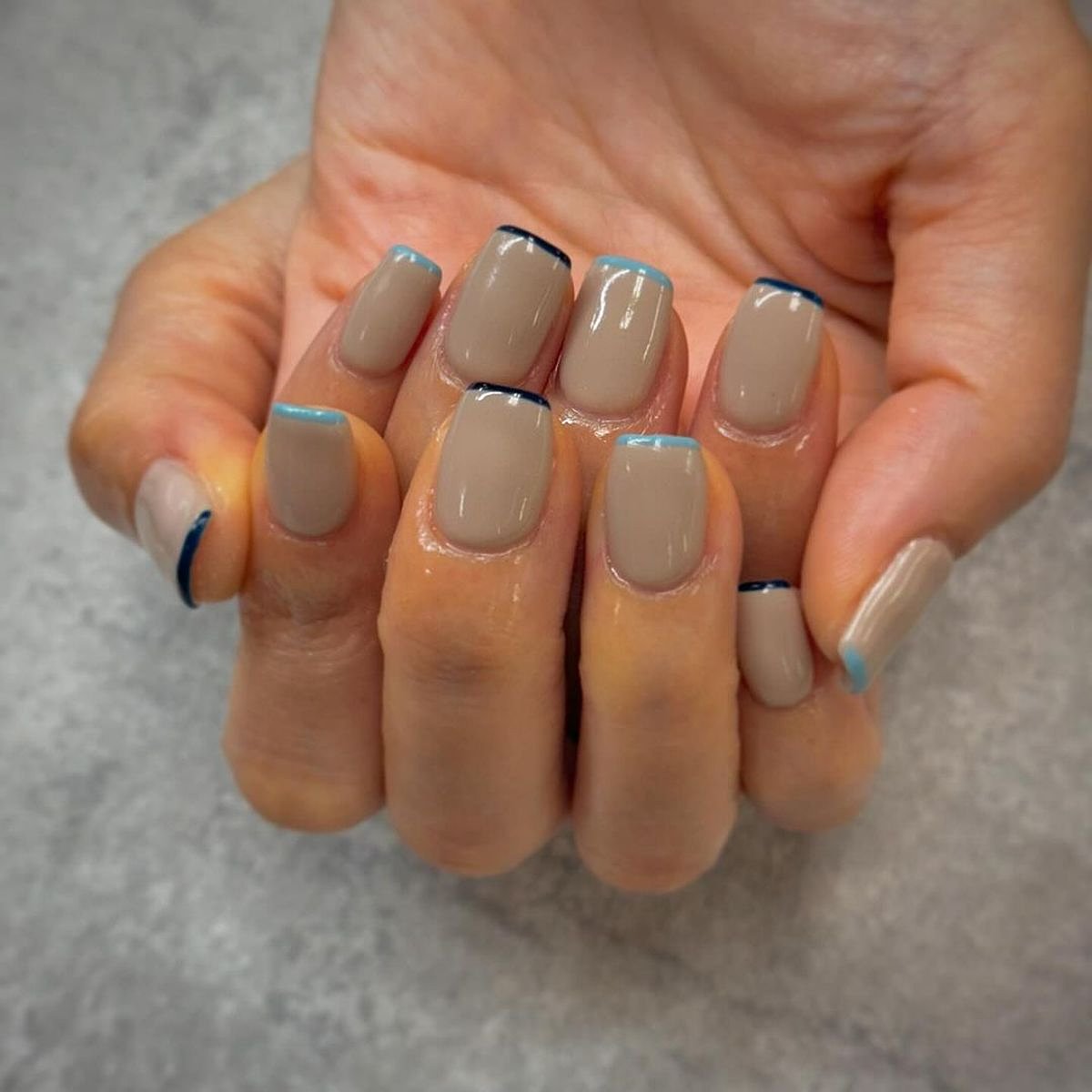 This image features a close-up of stylish nails painted beige with blue tips, showcasing a stylish manicure.