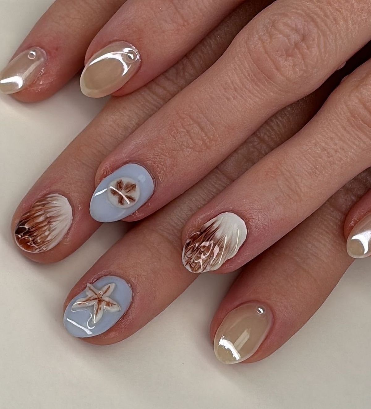 This image showcases intricate nail art featuring beige and blue colors with decorative patterns and designs.