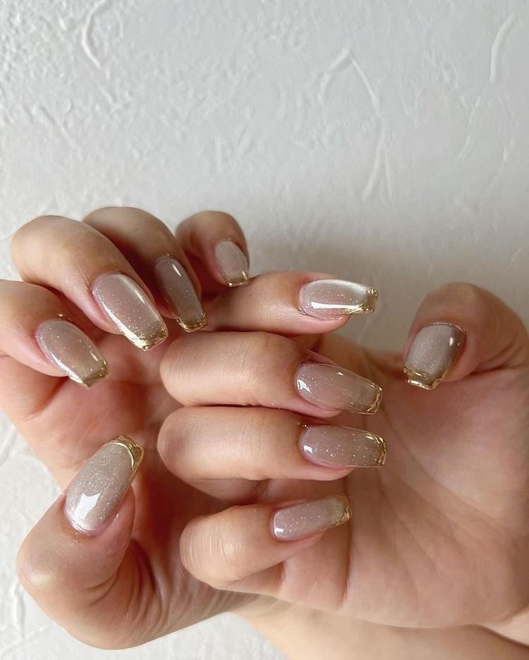 A close-up view of beautifully manicured nails featuring a beige base with gold glitter accents.