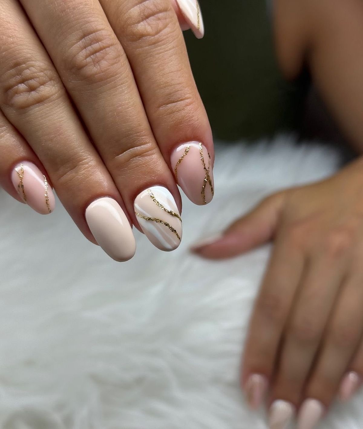 Close-up of elegantly designed beige and gold nails on a soft white background with delicate details.