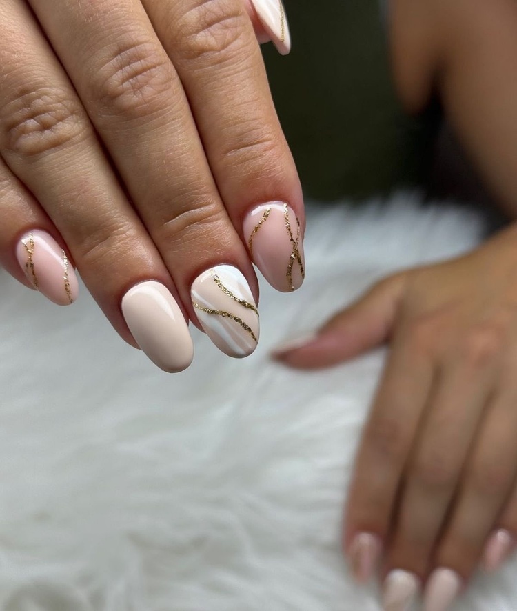 Close-up of elegantly designed beige and gold nails on a soft white background with delicate details.