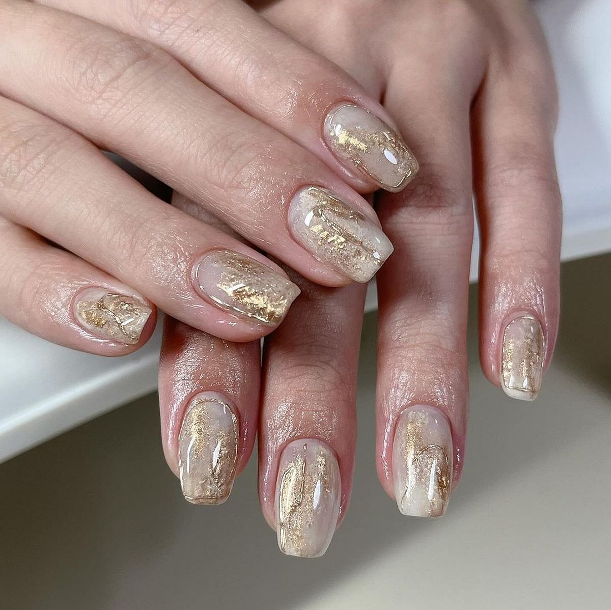 Stylish beige and gold nail design featuring intricate shimmer and glossy finish.