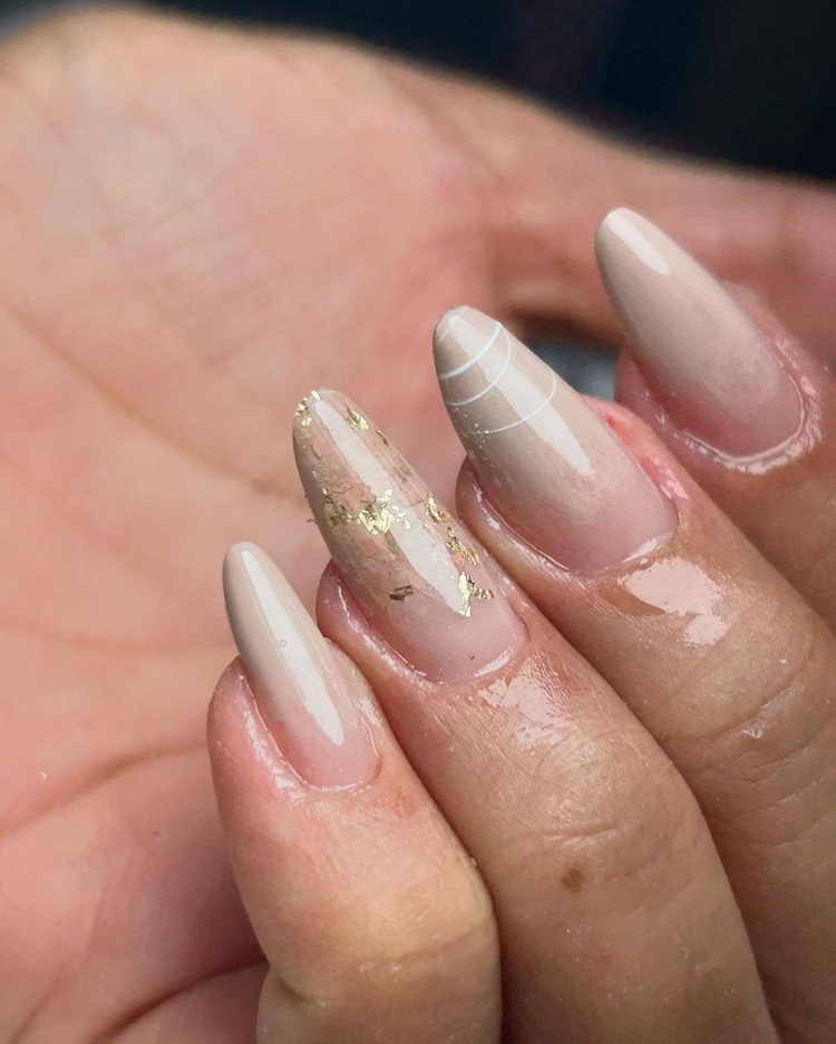 A close-up view of elegant beige and gold long nails, beautifully manicured with a glossy finish.