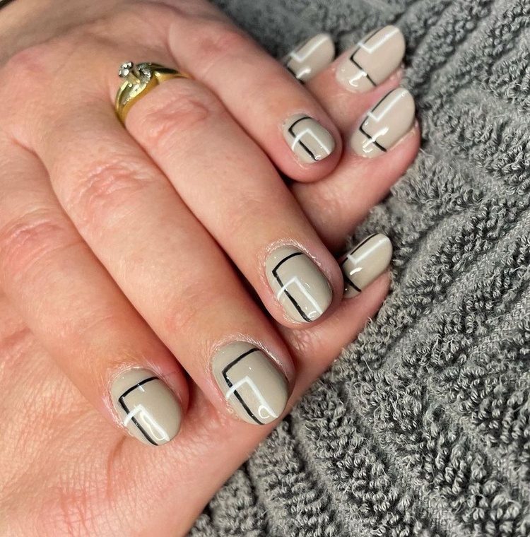 Close-up of manicured beige nails featuring black line art over a textured surface.