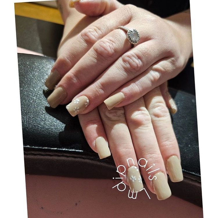 A close-up view of beautifully manicured beige nails featuring intricate nail art, set against a soft background.