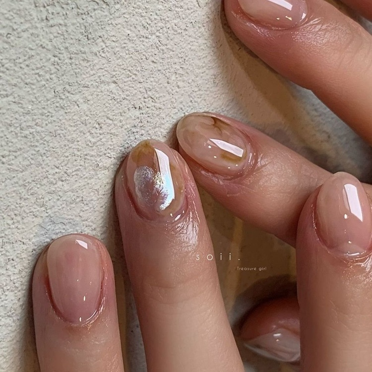 Beautiful nails with a glossy beige finish and gold accents, showcasing a sophisticated design.