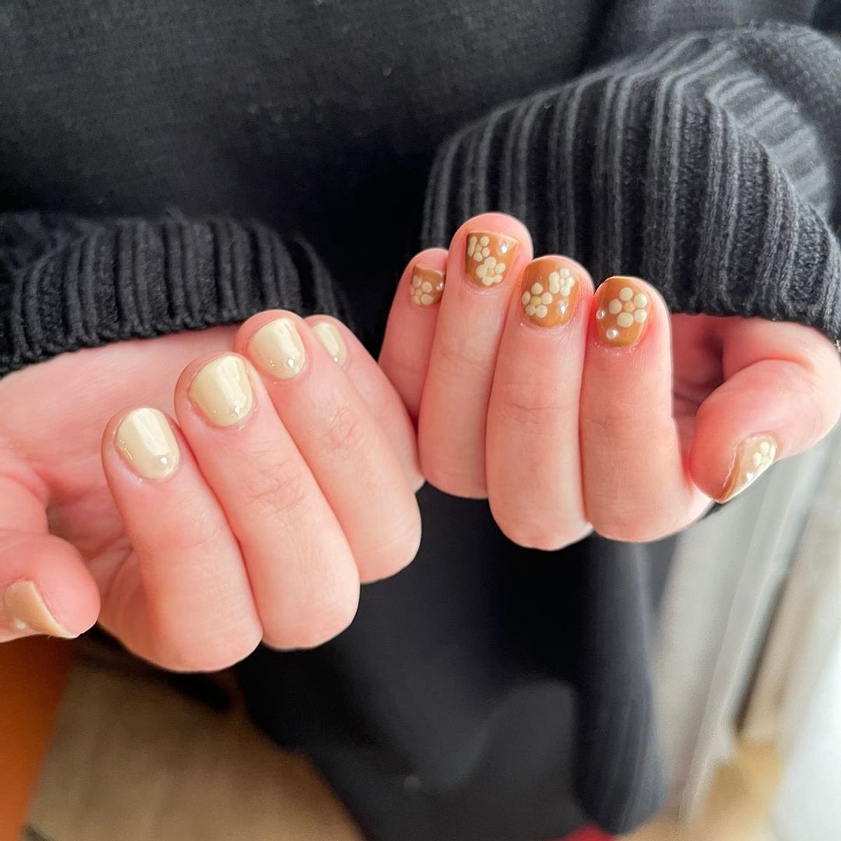 Stylish manicure featuring beige nails adorned with gold floral accents and dots.