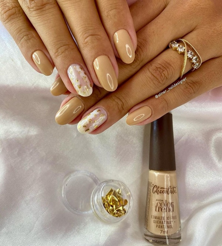 Elegant nails featuring a beige color with gold foil accents; beautifully manicured fingers against a soft backdrop.