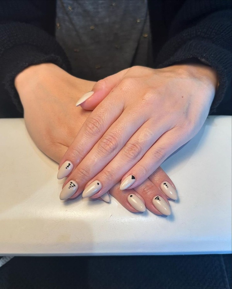 Beige long oval nails featuring unique artistic designs, beautifully manicured and well-groomed.