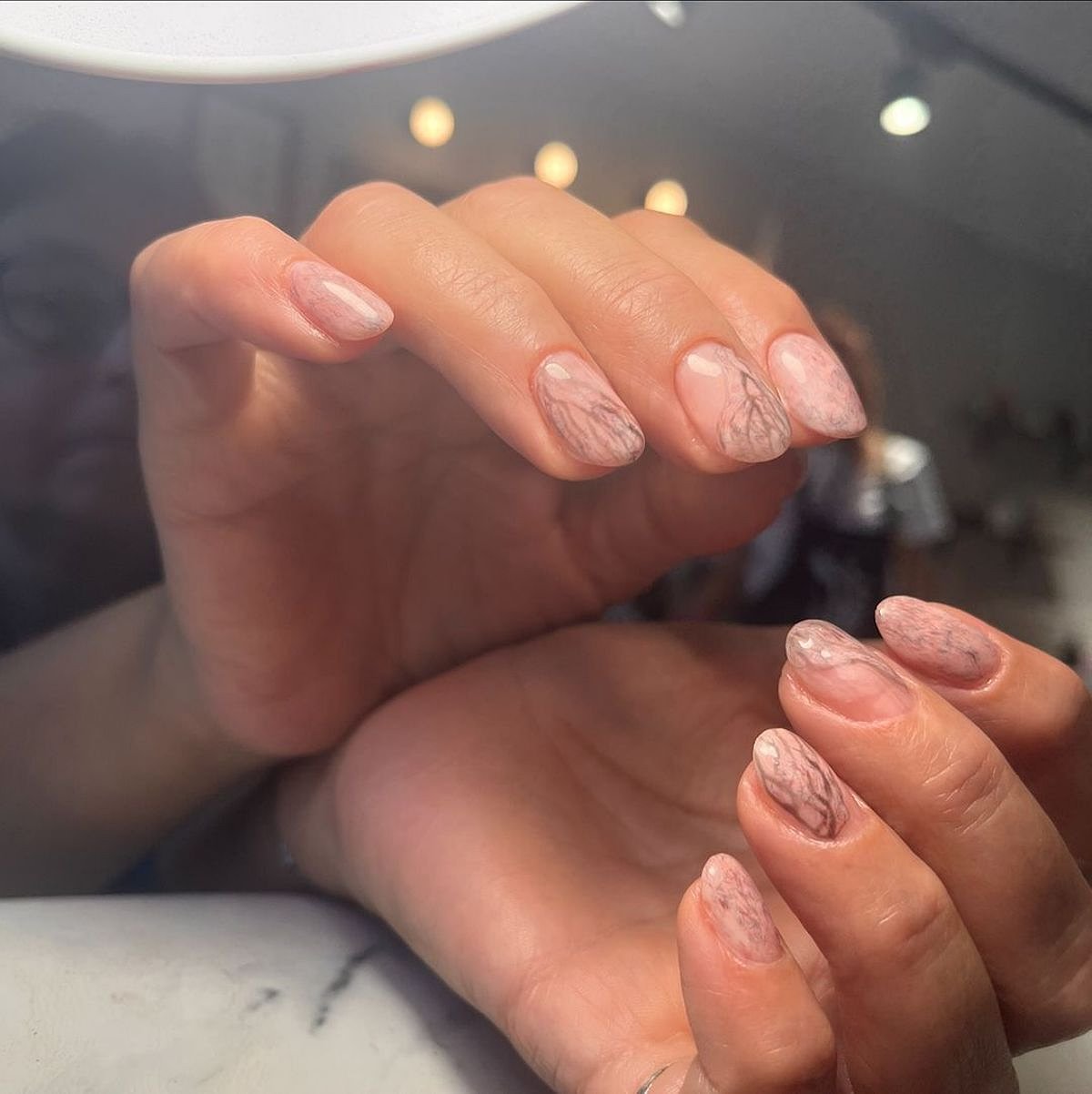 Beautiful elegant nails with a marble ombre effect in shades of beige, showcasing shimmer and gloss against a soft background.