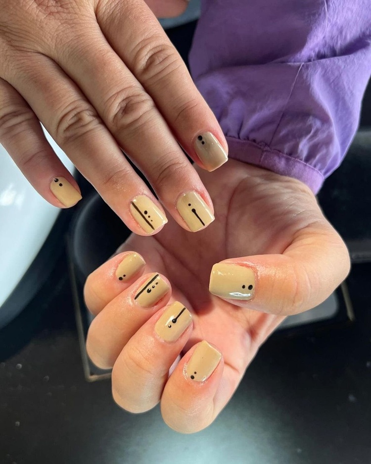 A close-up of stylish beige nails adorned with minimalist black dots and lines.