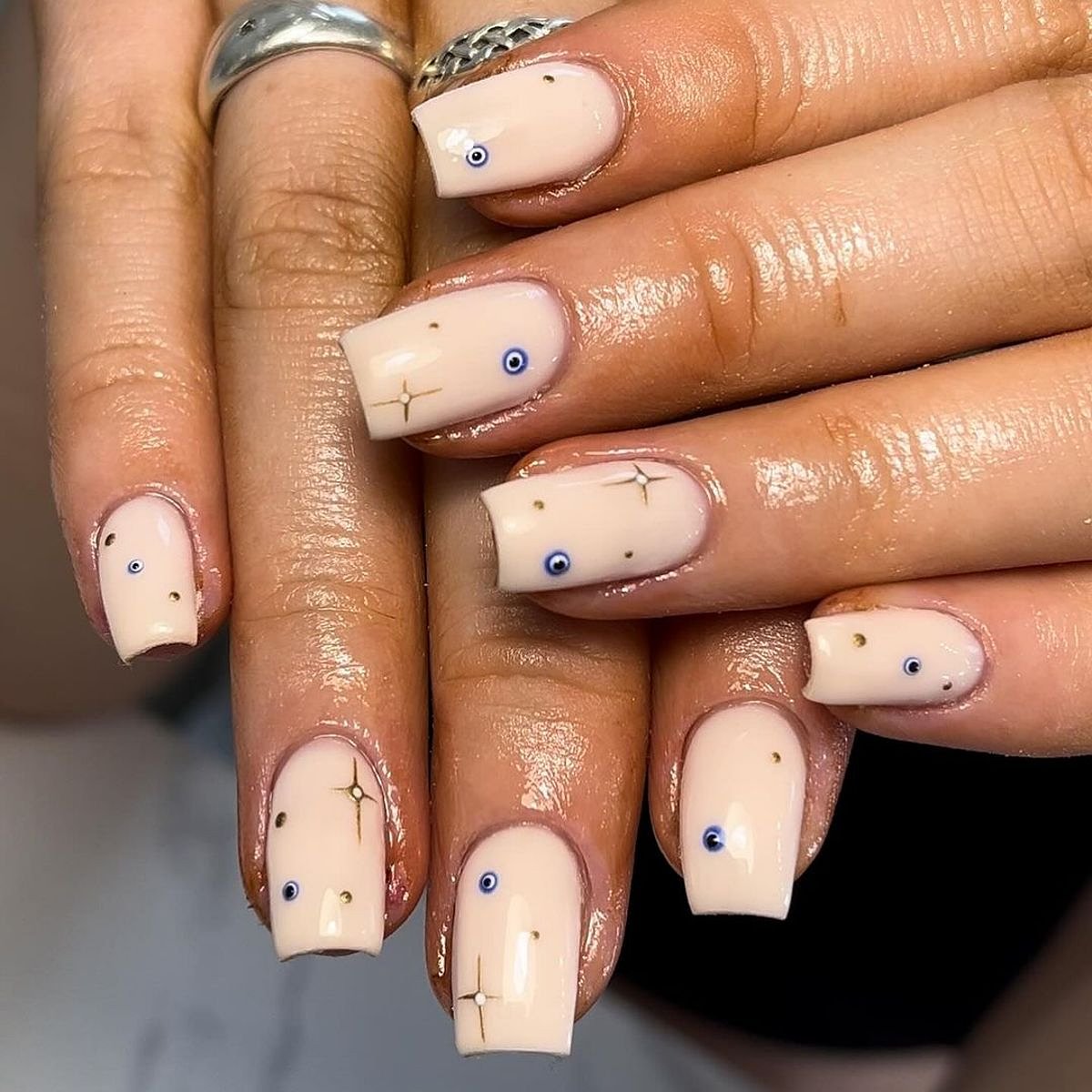 Close-up of elegant beige nails featuring evil eye designs and sparkling accents.