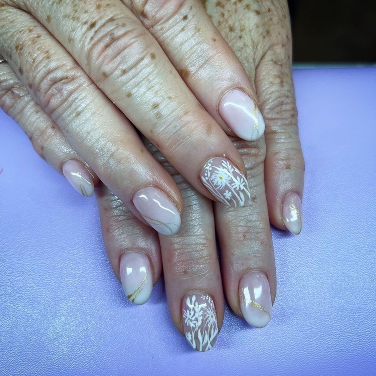 Elegant beige nails adorned with intricate white patterns, showcasing a refined manicure.