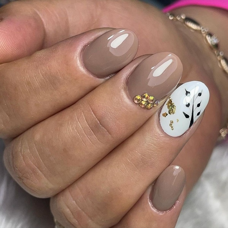 This photo showcases beautiful nail art featuring beige and white colors, enhanced with gold accents and decorative elements.