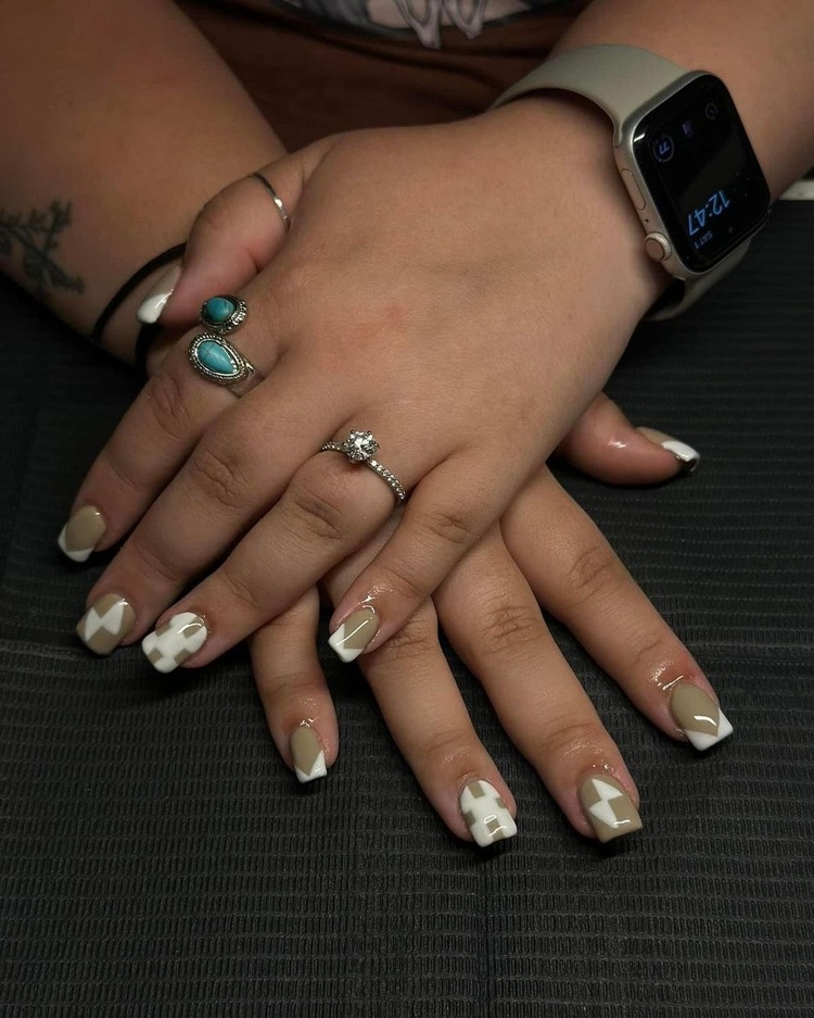 This is an image showcasing beautifully manicured beige and white nails with intricate designs, complemented by rings on fingers.