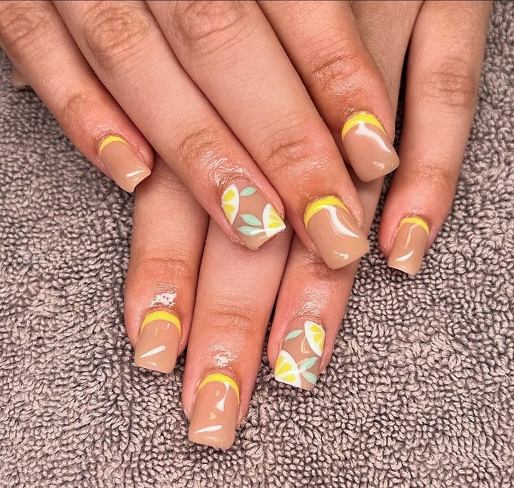 A close-up view of beautifully manicured beige nails featuring yellow tips and delicate leaf designs.