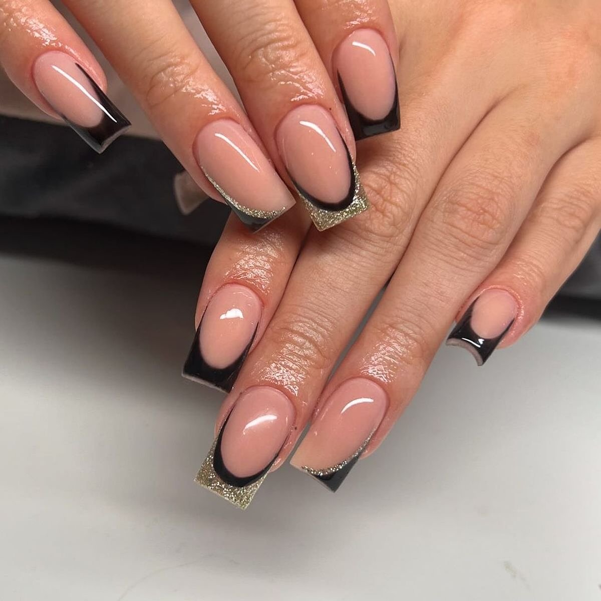 Four elegant fingers showcasing black and beige gel nails in a modern design against a soft background.