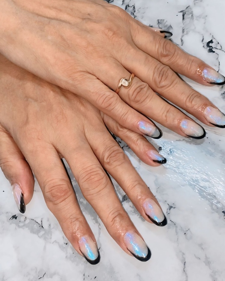 Close-up of hands displaying elegant black and blue holographic nails on a marbled surface.