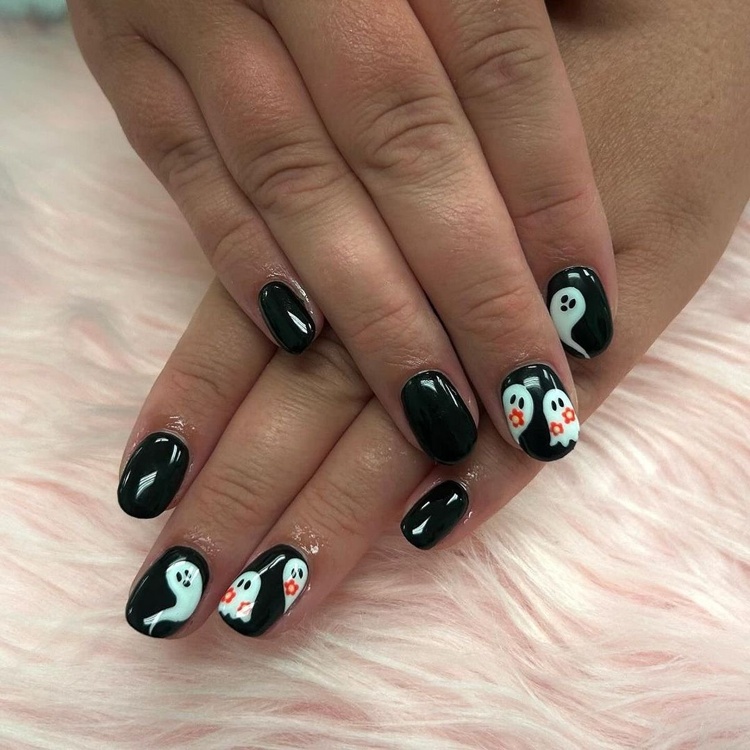 Black nails featuring ghost designs with orange accents, perfect for Halloween.