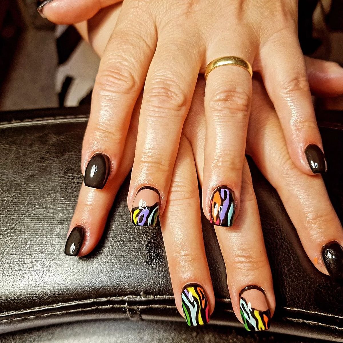 Close-up view of beautifully manicured nails featuring a black base with colorful stripes and artistic designs.