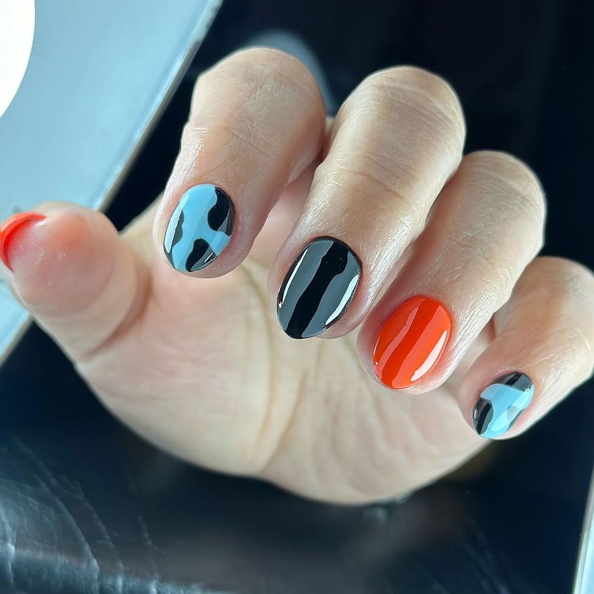 A hand showcasing black, orange, and blue nails with a polished finish.