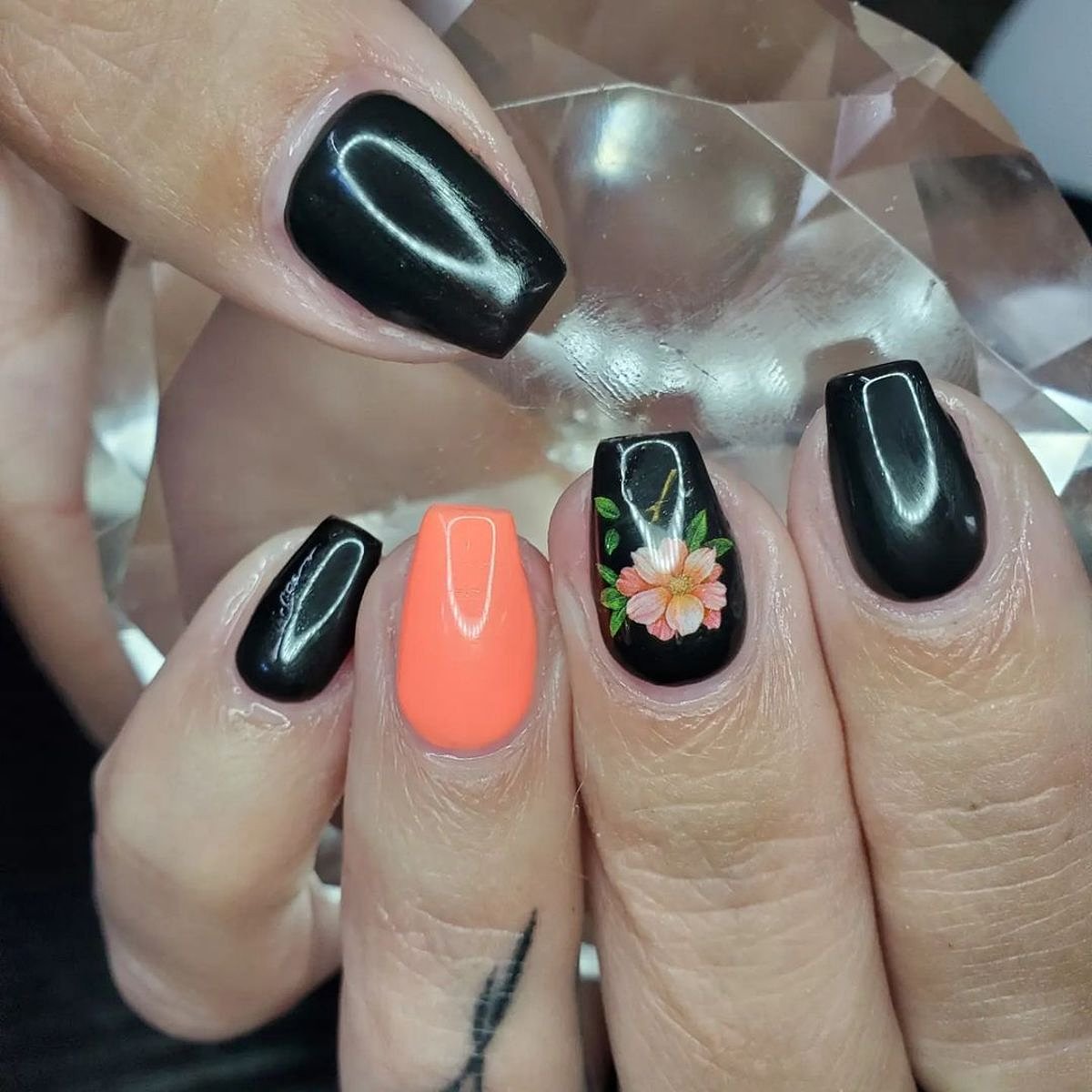 Showcasing beautiful black and orange nails with floral accents, set against a shimmering background.