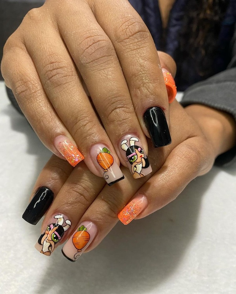 Close-up of beautifully manicured nails featuring black and orange colors with intricate designs and glitter.