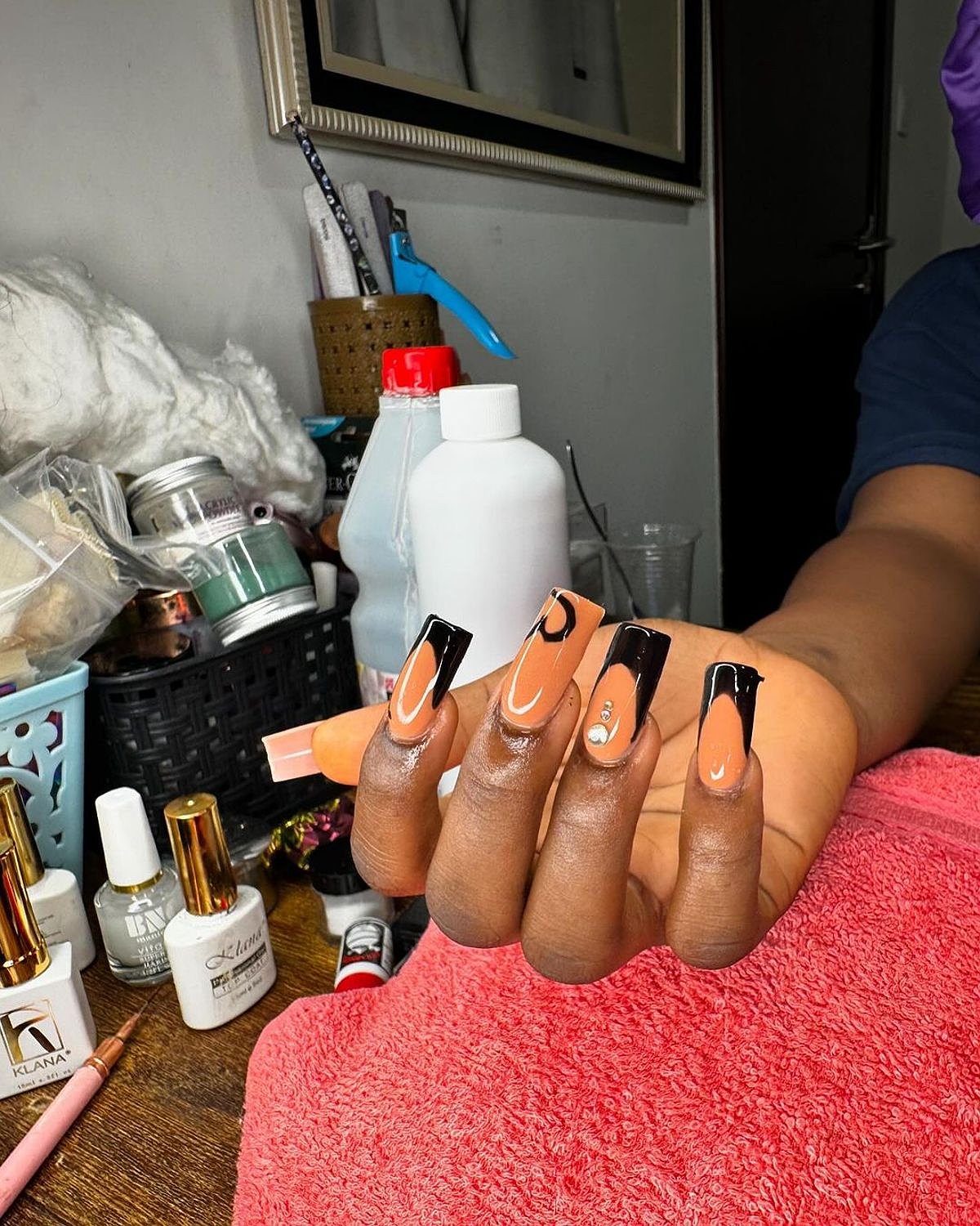 Long black and orange nails with stylish designs, set against a cozy background with nail care products.