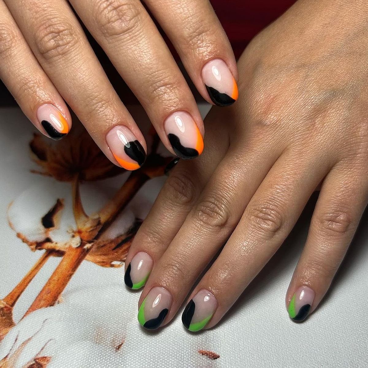 Elegant manicure featuring black, orange, and green nail art on nude base with well-groomed fingers.