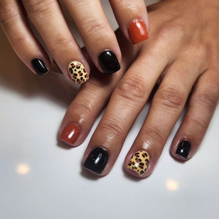 Close-up of beautifully designed black and orange leopard print nails with a glossy finish.