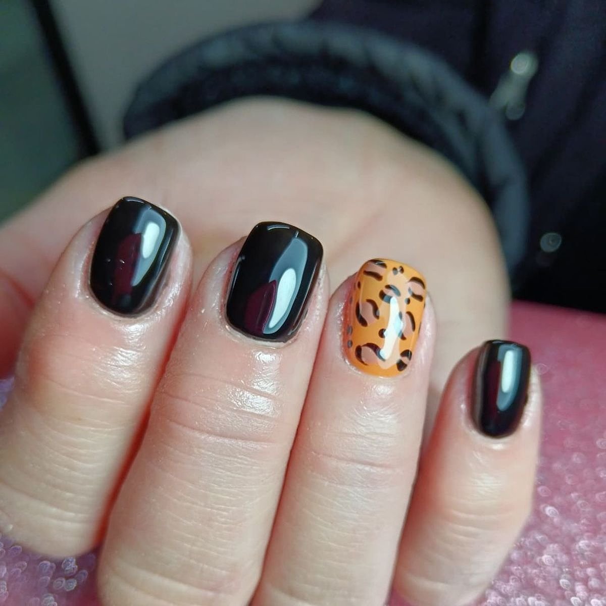 Glossy black and orange nails featuring a leopard print accent nail, showcasing a stylish manicure.