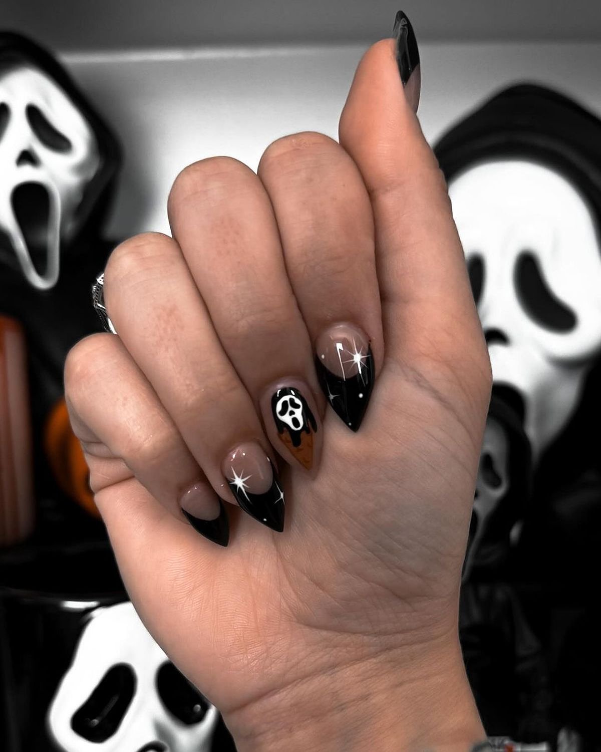 Stylish black and orange nails featuring a shiny dog paw design, held by a hand against a spooky background.