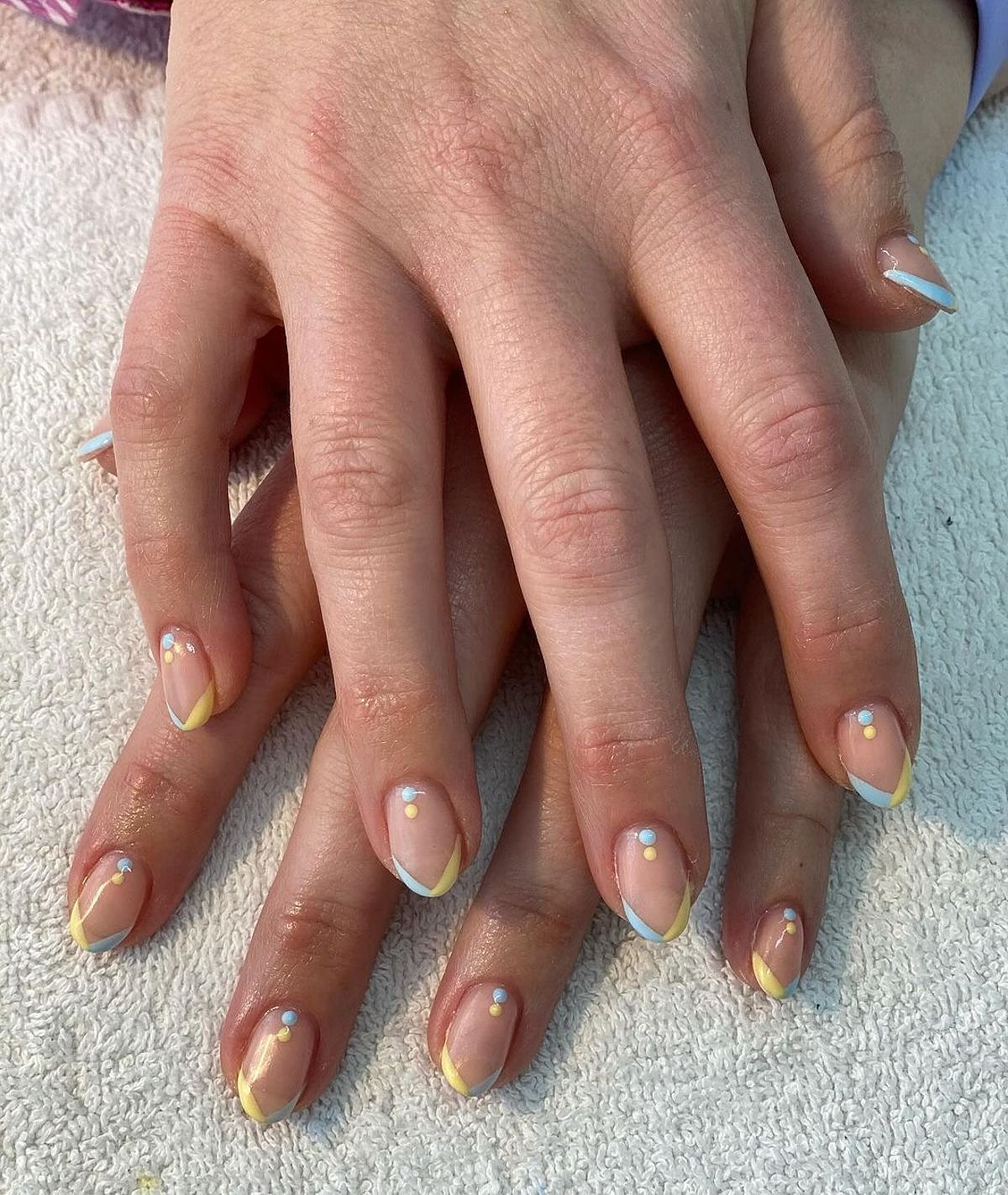 Chic nails adorned with a beautiful yellow and white design and sparkling gem accents. Stylish nails featuring a chic yellow and white design with elegant gems, resting on a soft towel.