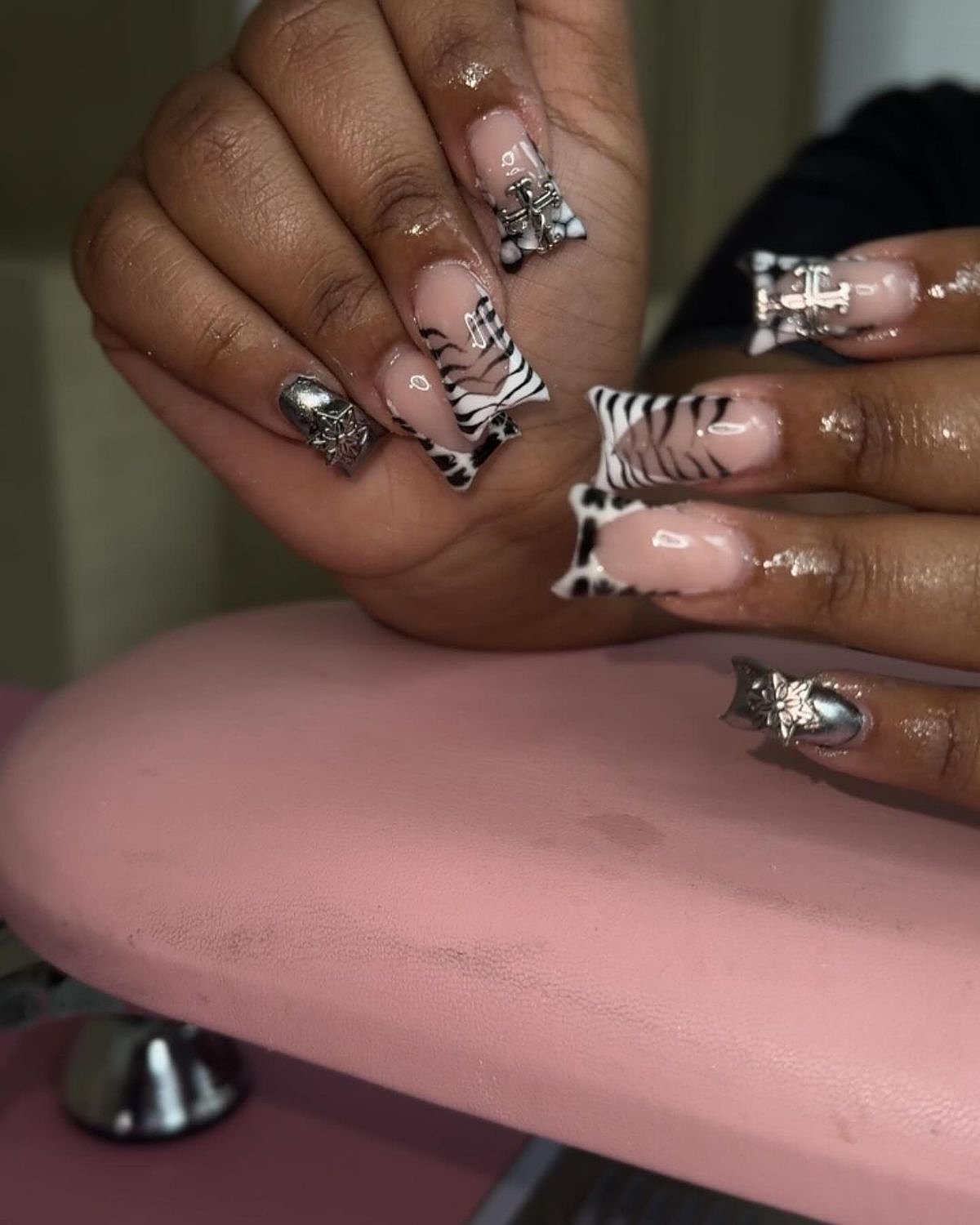Gorgeous pink and black zebra-inspired nails adorned with shimmering details and elegant designs. Close-up of stylish pink acrylic nails featuring black and white zebra patterns, glitter accents, and decorative elements.