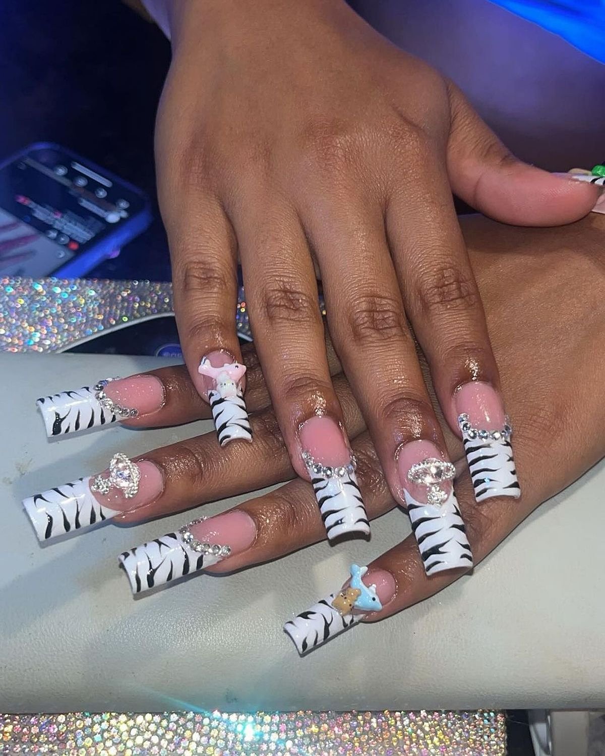 This image showcases beautifully manicured zebra print nails adorned with pink gems and jewelry. The vibrant nails capture attention effortlessly.