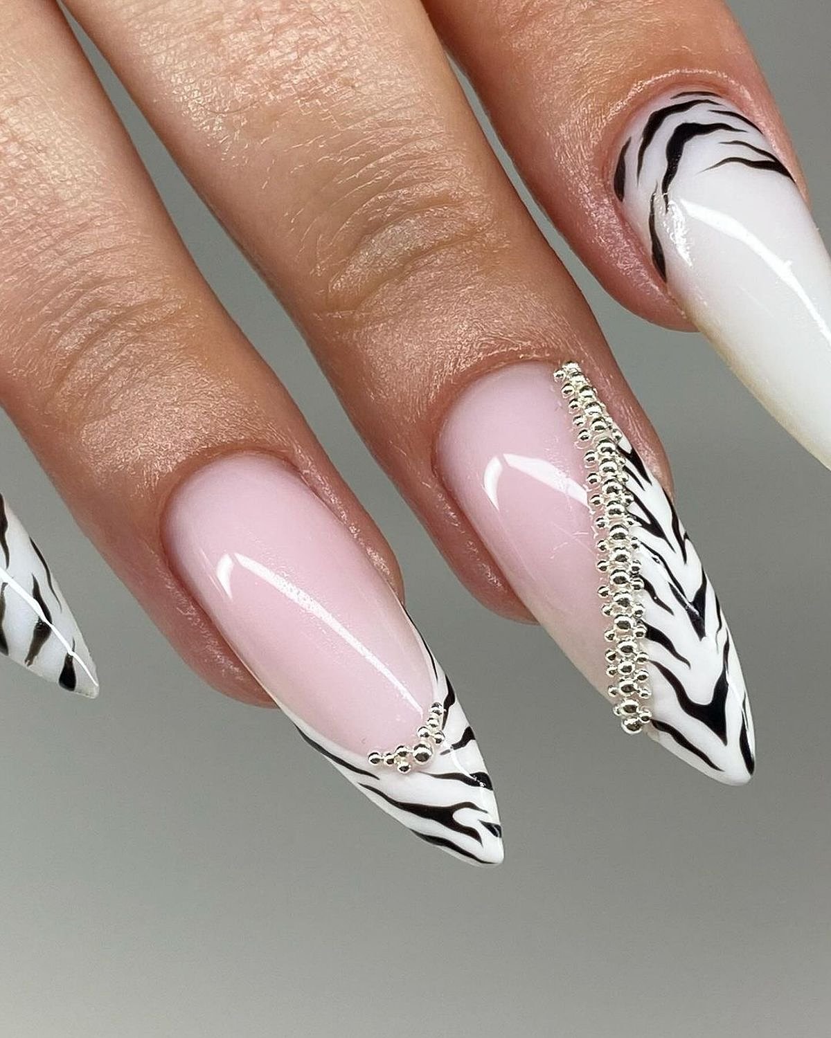 A close-up of elegant long stiletto nails featuring a zebra print and gem detailing against a neutral background.